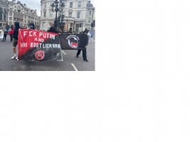 4 people stand ahead of demo with banner saying FCK PUTIN & HIS BOOTLICKERS with anarchy symbo...png