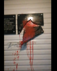 black plaque smashed with red paint on it dripping down on white wall