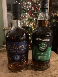 A bottle of Glen Allachie 15 sits next to a Springbank 15 on an attractive table. There’s an out of focus Christmas tree in the background.