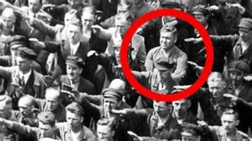 Iconic picture of a man standing with his arms folded while those around him perform the Nazi salute. 