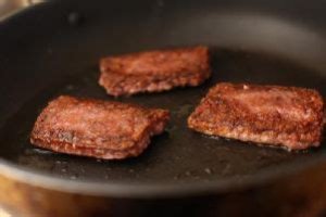 Three square sausages sizzling in a pan. 