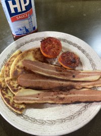 Fried veggie bacon rashers, tattie scones and tomatoes sir on a plate. In the background is a bottle of HP sauce.