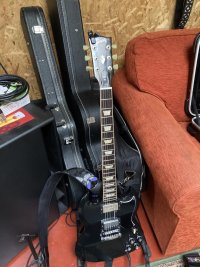 An ebony Gibdon SG Standard on a guitar stand amongst rehearsal room clutter.