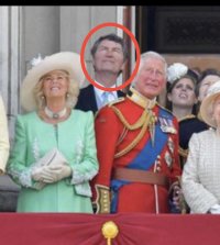 A crop of the photo in question. A man stands behind Camilla and Charles on the Royal balcony. I have ringed him in red. He looks inbred and might well be a cousin or lover or both. 