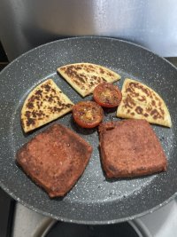 A frying pan sizzles away with square sausage, tattie scones and tomatoes.