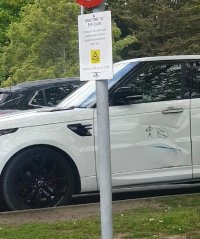 A parked white Range Rover, with a big scrape and dent in the passenger door, pn which someone has drawn a stick figure with its arms up and a speech bubble saying what bollard!