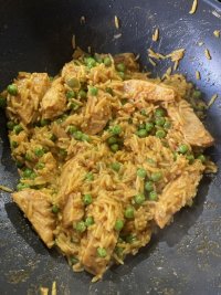 A frying pan containing vegan chicken pieces, rice, peas, with herbs spices and so on. 