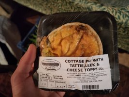 A small pie with pastry sides and base, and potato on top. The label says cottage pie with tattie, leek and cheese topping