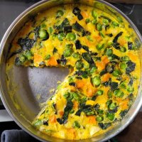 A large pan of frittata with one slice cut out. It contains broad beans, squash and chard and all the colours are really bright and fresh.