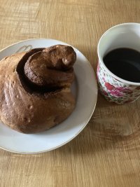 A large cinnamon bun on a plate next to a cup of coffee.