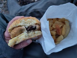 I'm holding a cheese scone made into a sandwich with a battered slice of black pudding in the middle. There's a bag of chips on my lap.