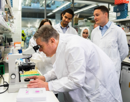 Keir Starner in lab coat looks through microscope.png