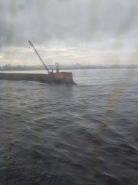 A small lighthouse next to a big crane, at the end of a long concrete pier sticking out into the sea