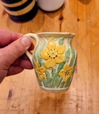 A very small, attractive cream vase with daffodils on