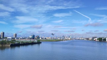 View from a bridge over the Thames, looking west towards London City Airport just as a plane leaves the runway.