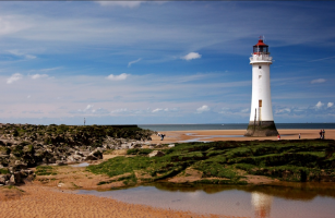 white lighthouse on sandy beach under a blue sky