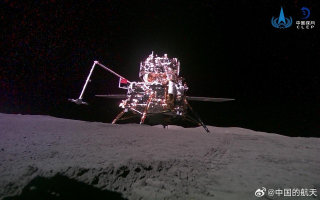 View of lander (robotic sampling arm in action) as seen from the rover.