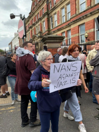 Woman in front of some other ppl holds sign NANS AGAINST NAZIS 