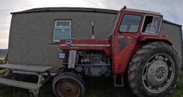 a red tractor parked beside a pebbledashed building in Orkney