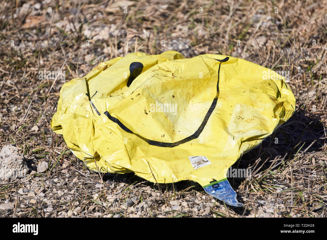 empty-deflated-mylar-smiley-face-yellow-balloon-on-the-ground-outside-T2DH28.jpg