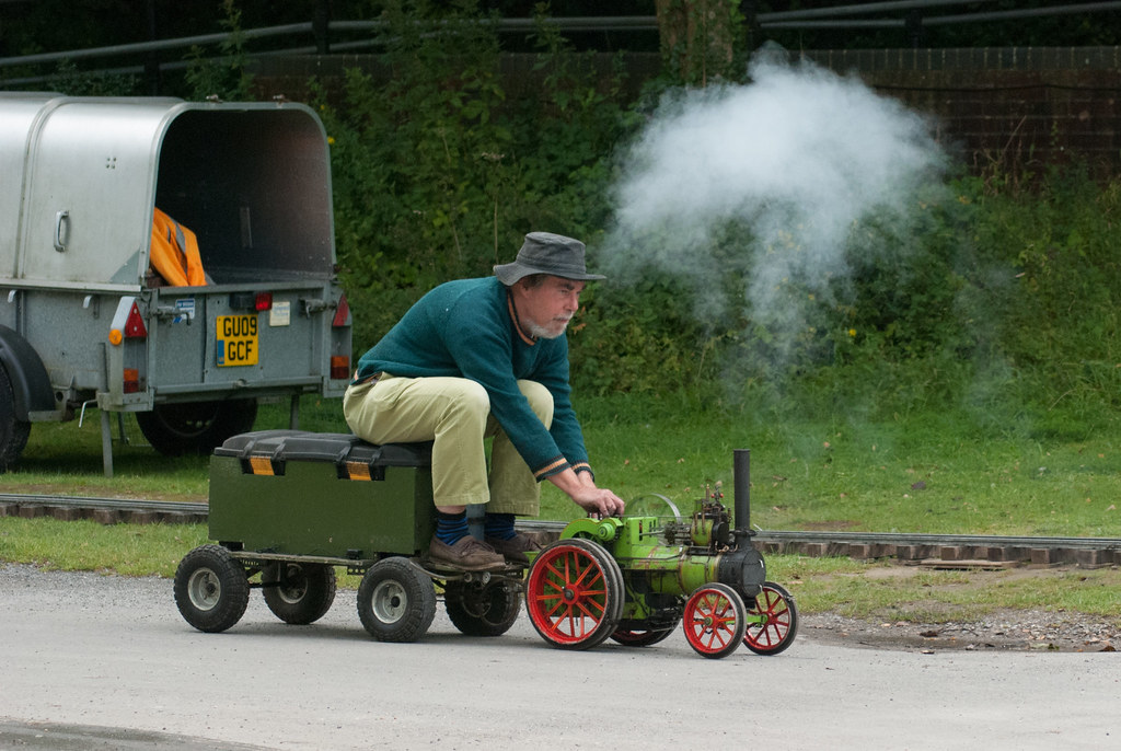 man sat on a trolley being pulled by a mini steam engine